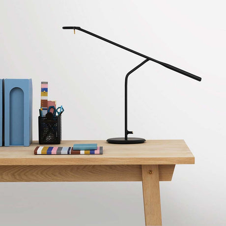Elegante LED Tischlampe Flow in Schwarz auf einem Holzschreibtisch mit Büchern und Bürobedarf.