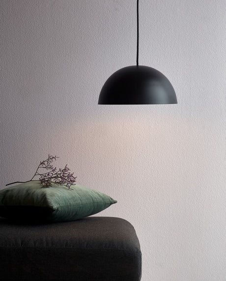 Hängelampe Ellen 30 Schwarz über einem Tisch mit grauer Decke und grünen Kissen, minimalistisch und skandinavisch.