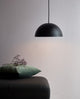 Hängelampe Ellen 30 Schwarz über einem Tisch mit grauer Decke und grünen Kissen, minimalistisch und skandinavisch.