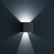 LED Außen-Wandlampe Siri 44 - L IP54 Schwarz an einer Wand mit sanftem Lichtstrahl.