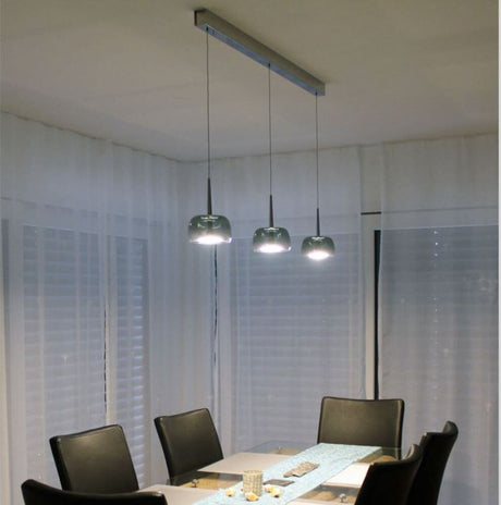 LED Lampe à suspension Flute chromée avec trois luminaires au-dessus d’une table à manger dans un environnement moderne.