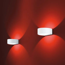 Deux LED appliques murales Fosca blanches sur un mur rouge, diffusant une lumière chaleureuse.
