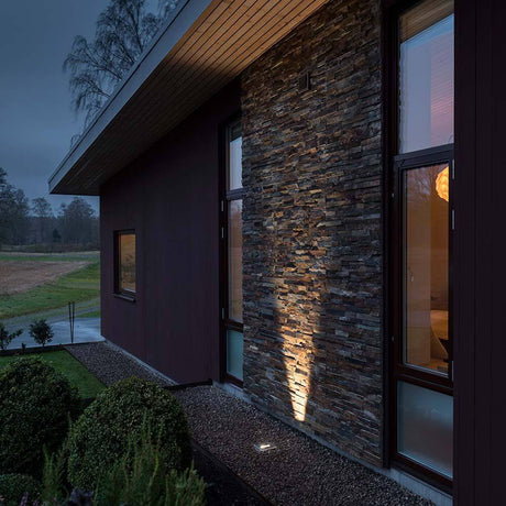 O projetor de chão LED com saída de luz ajustável em aço inoxidável ilumina uma fachada de casa moderna.