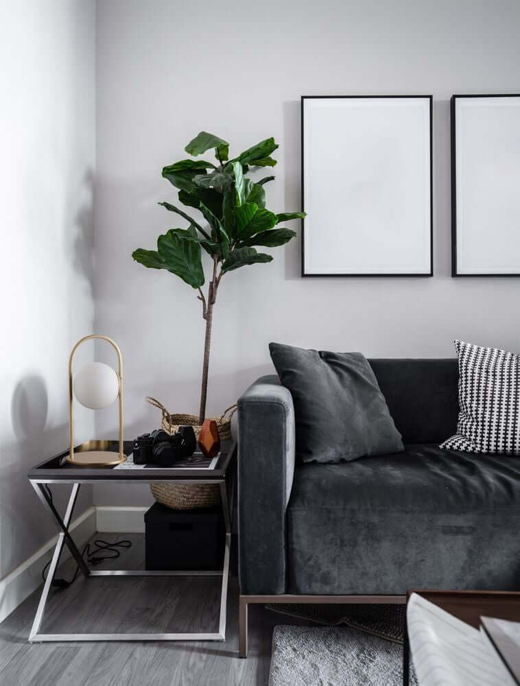 Hook LED Tischleuchte 3000K Gold-Gebürstet, Weiß neben Sofa mit Pflanze und Bildern an der Wand.