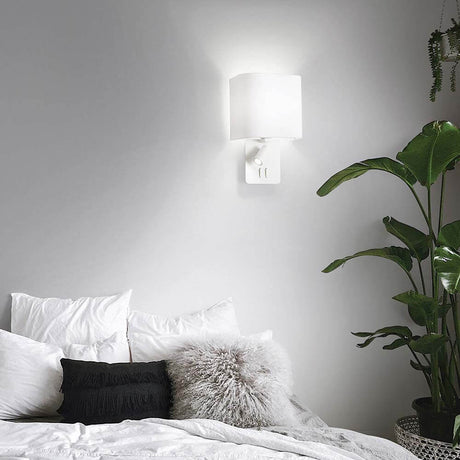 Gea Map væglampe med LED Læselys på en væg over et bed dekoreret med planter.