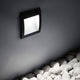 LED Außen Wandleuchte IP65 an einer Wand über weißen Kiessteinen montiert.
