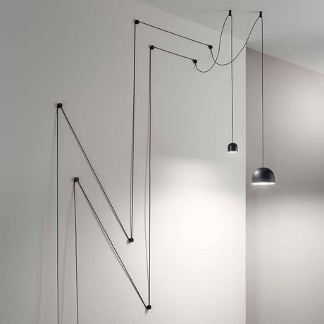 Pendelleuchte Tall Groß Schwarz mit innovativer Kabelaufhängung an einer Wand.