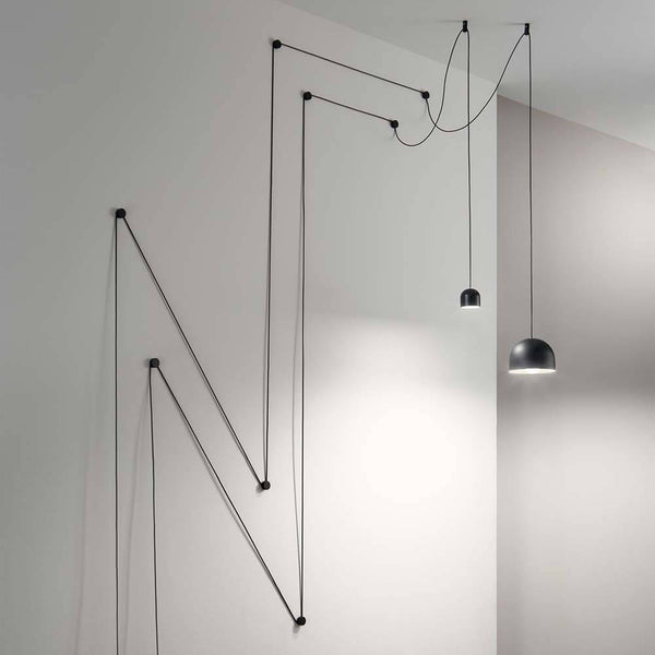 Pendelleuchte Tall Groß Schwarz mit innovativer Kabelaufhängung an einer Wand.