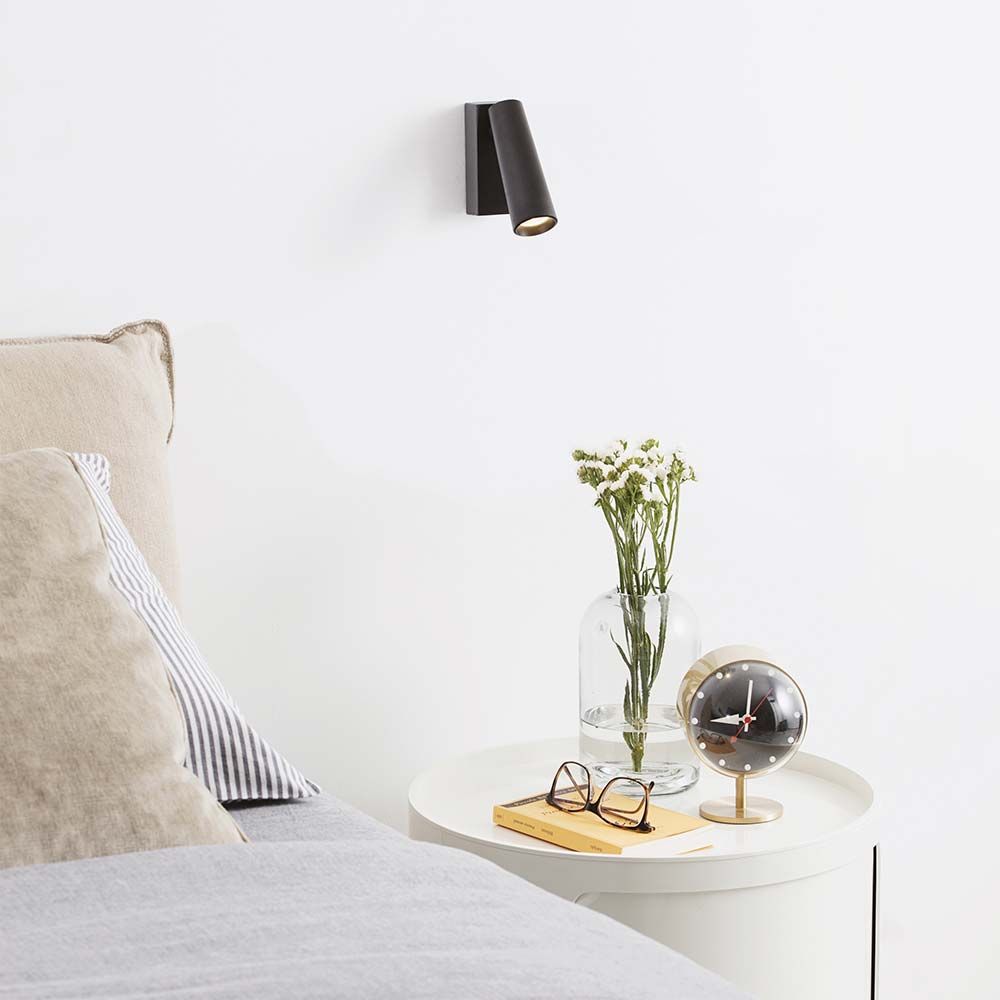 Pipe LED Wandleuchte Strahler in modernem Schlafzimmer neben Tisch mit Blume und Uhr.