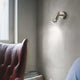 Wandleuchte Alfa Ap1 Brüniert an einer Wand über einem roten Sessel, modern und stilvoll.