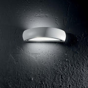 Wandleuchte Giove Ap1 Weiß an einer rauen Wand, moderne und elegante Beleuchtungslösung.