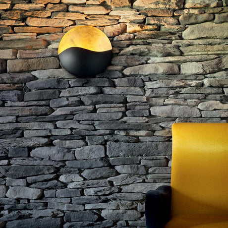 Sunrise Ap3 wall light in black E Oro on a stone wall with a yellow sofa