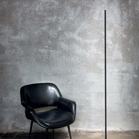 Yoko LED floor lamp metal next to a modern black chair in front of a gray wall.
