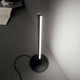 Yoko LED Tischleuchte Metall auf einem Tisch, modernes Design mit schmalem Lichtstreifen in Schwarz.