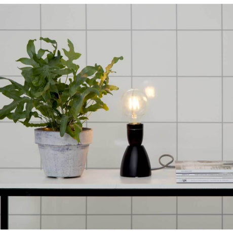 E27 LED Filament 2100K 140lm Dimmbar in einer modernen Tischlampe mit Pflanze auf einem Tisch.