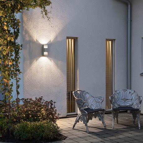 Imola LED Außen-Wandleuchte Style Design Grau, opales Acrylglas an einer Hauswand mit Gartensitzmöbeln.