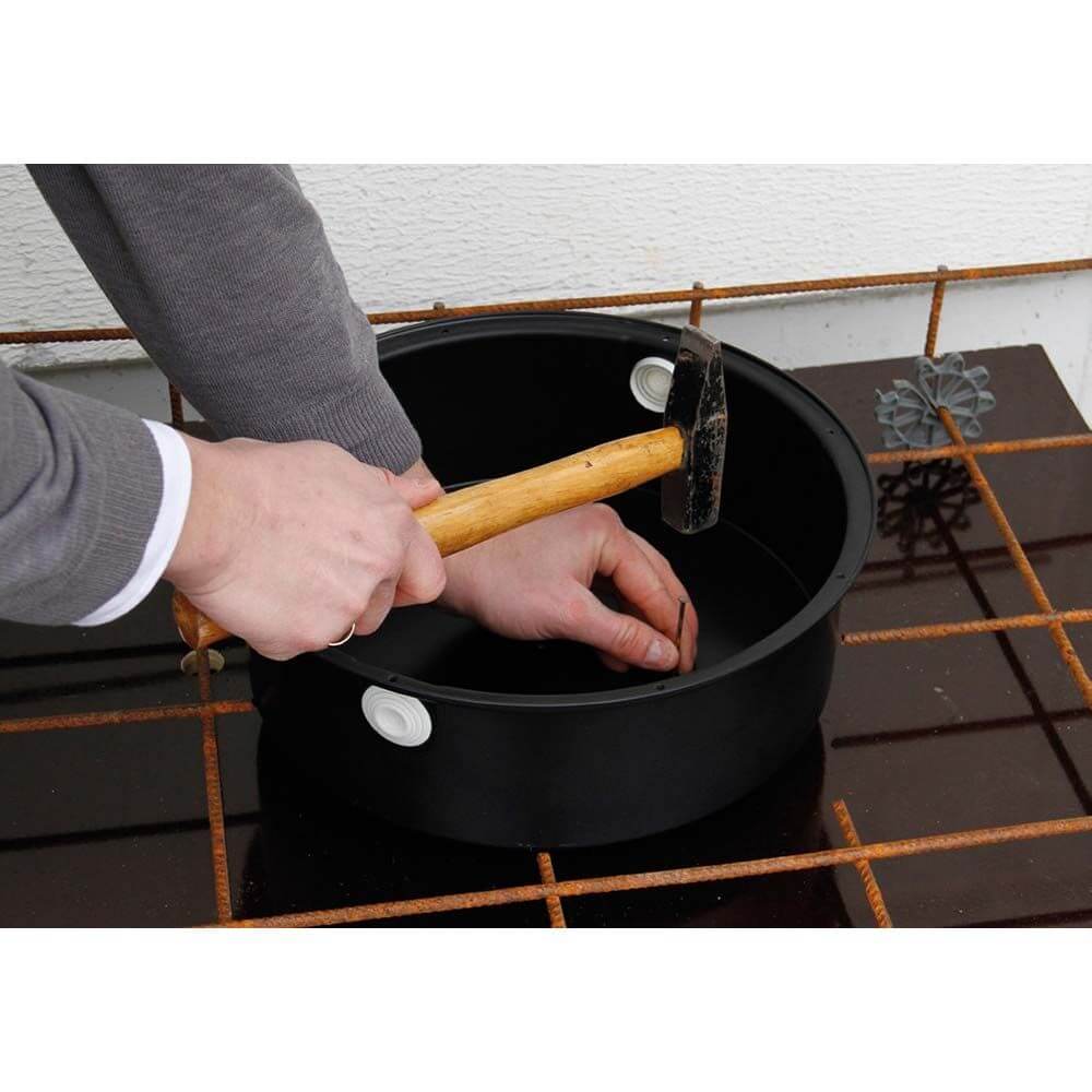 Hände schlagen auf die Individuelle Leuchten-Einbaudose XXL Ø 310mm für Betonbau mit einem Hammer.