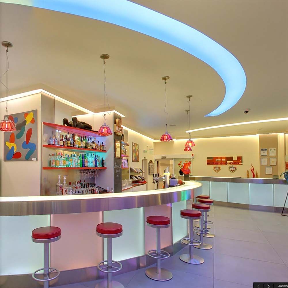 Moderne Bar mit beleuchtetem Thekenbereich und buntem Hintergrund, ausgestattet mit roten Barhockern.