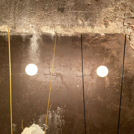 Ingo Maurer Stehlampe Ilios Designklassiker mit rundem Opalglas und langen Metallstäben an Wand.