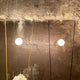 Elegante Ingo Maurer Stehlampe Ilios mit runder Opalglas-Glühbirne und schlanken Metallstäben vor einer rustikalen Wand.