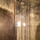 Elegante Stehlampe Ilios von Ingo Maurer mit Opalglas und metallenen Stäben vor einer rauen Wand.