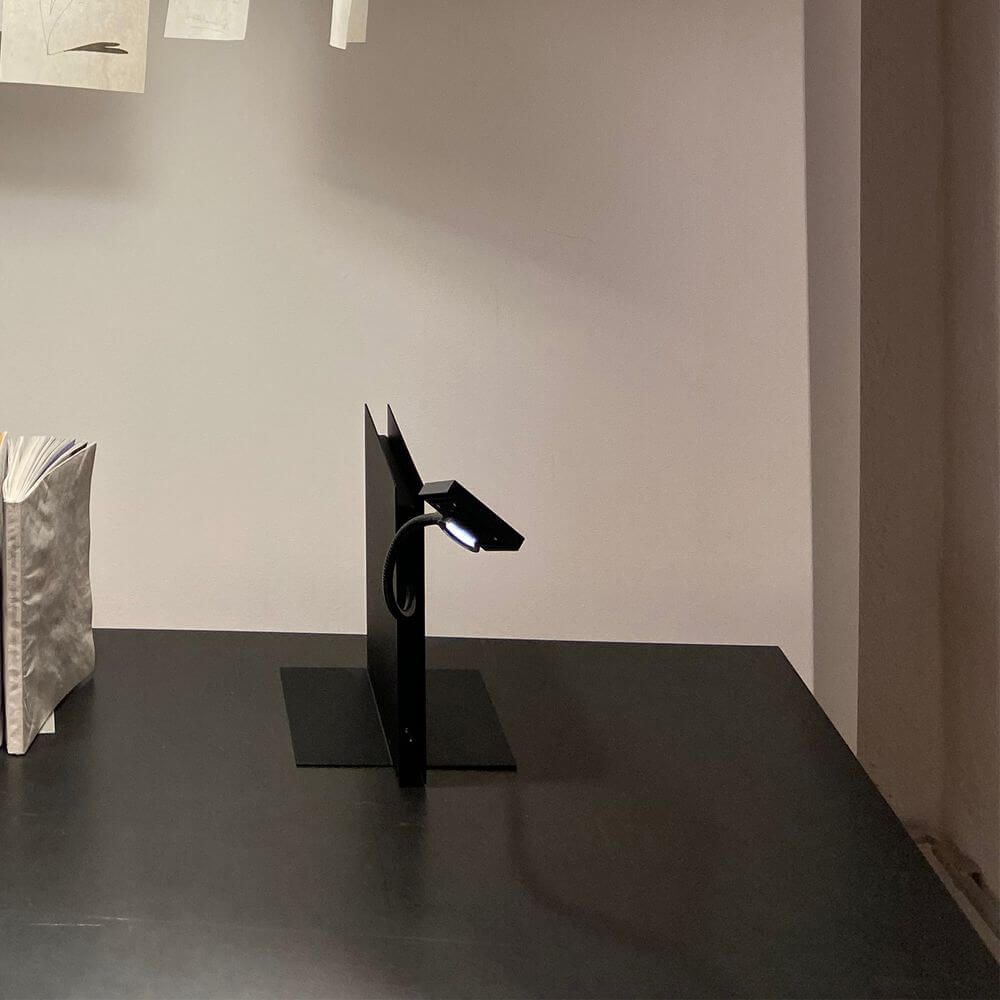 Ingo Maurer Tischleuchte LED's Oskar in Schwarz als moderne Buchstütze auf einem Tisch.