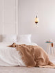 Intra Wandleuchte Natur, Schwarz über einem gemütlichen Bett mit beige Decke, die Wärme und Eleganz vermittelt.