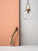 Irvine Pendelleuchte Ø 20cm Gold, Transparent an einer modernen Wand mit Blumenvase.