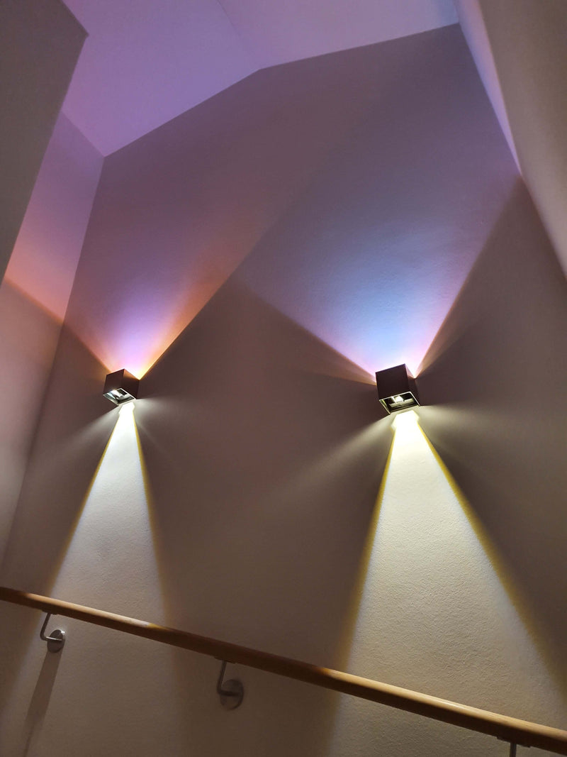 Moderne Wandleuchten strahlen farbiges Licht im Treppenhaus aus.