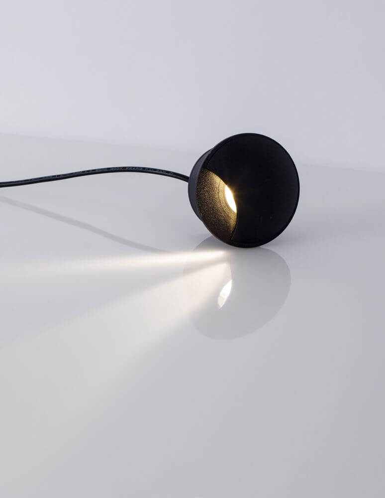 Joya LED Außenwandeinbauleuchte Up 3000K Schwarz IP65 auf einem Tisch mit Lichtstrahl.