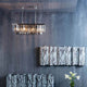 Hängeleuchte Smoky Lounge Rectan mit facettierten Glaskristallen über Wandrelief und Blumenarrangement.