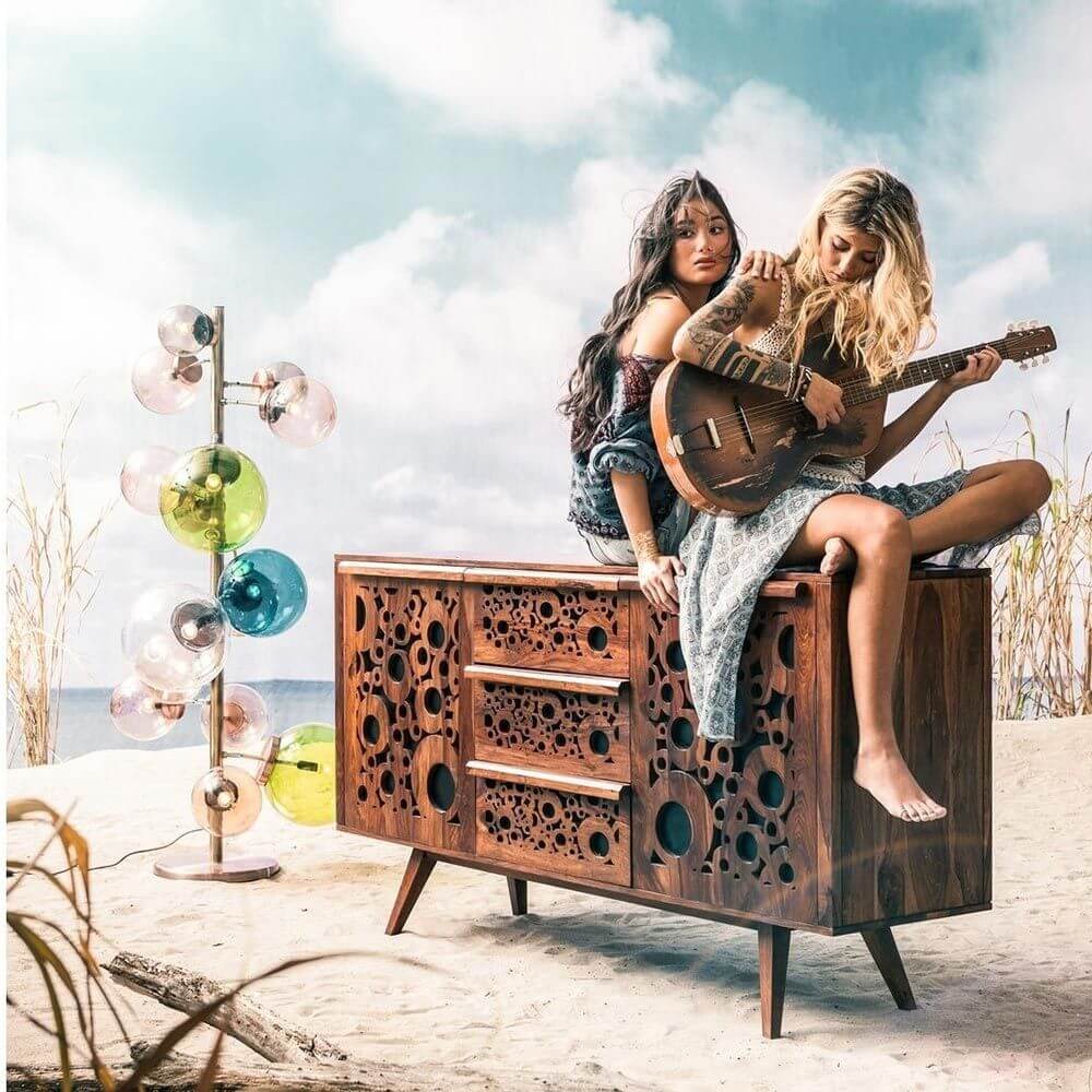 Zwei Frauen spielen Gitarre auf einem Holzmöbel vor einer Kugel-Stehleuchte Balloon Colore 160cm und einem hellen Himmel.