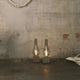 Karman Amarcord Tischlampe in Rauchglas-Optik auf rustikalem Tisch, elegante Lichtquelle für jeden Wohnbereich.