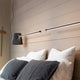 Karman Cupido Schirm für Cupido LED-Balkenlampe über einem Bett mit dekorativen Kissen.