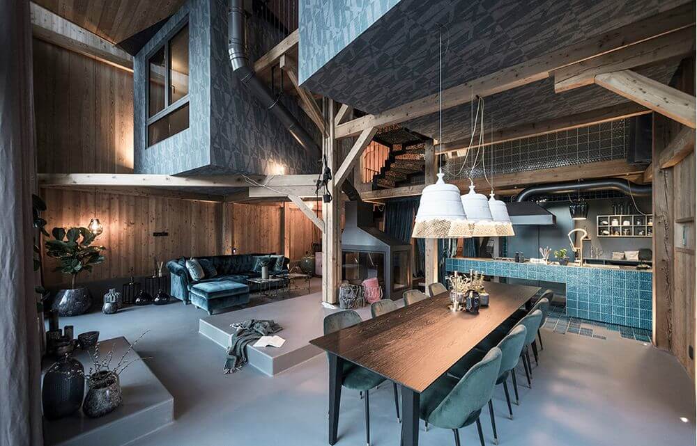 Innenansicht eines modernen Wohnraums mit Holz, einer langen Esstischgruppe und Hängelampen.