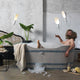 Mann entspannt in einer Badewanne mit Karman Workinprogress Hängeleuchte Weiß im Hintergrund, umgeben von Pflanzen.