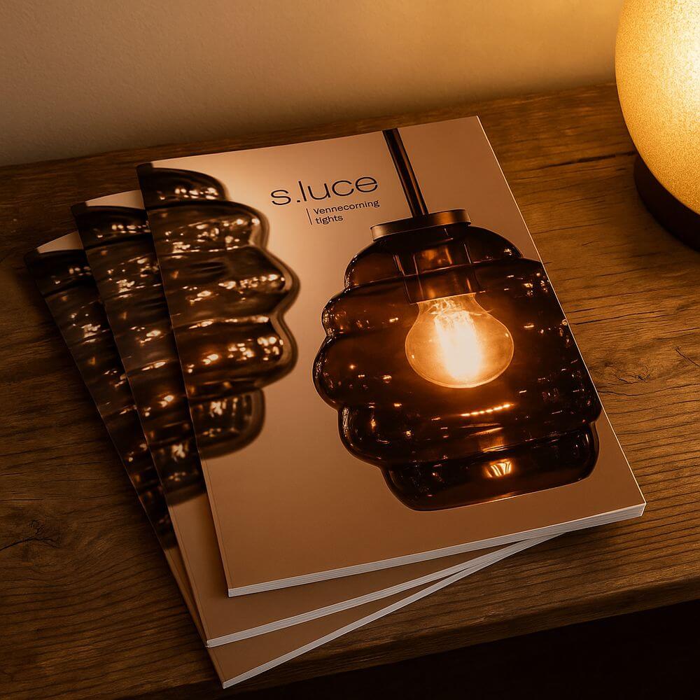 s.luce® Katalog homecoming lights auf einem Tisch mit stilvollen Leuchten und warmem Licht.