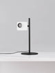 Kedros LED Tischleuchte 3000K mit Lampenfuß auf einem Tisch, moderne Designleuchte in Schwarz und Weiß.