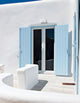 Hellblau gestrichene Fensterläden vor einer weißen Wand, mit einem modernen Balkon im mediterranen Stil.