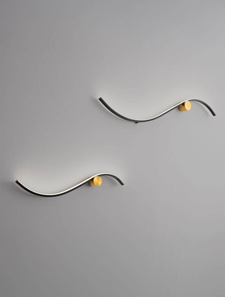 Kima LED Wandleuchte Geschwungen 3000K Schwarz, Gold an einer grauen Wand installiert.