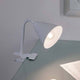 Klemmlampe Vitis mit Flexarm Schnurschalter Weiß auf einem Tisch mit Flexarm und weißem Lampenschirm.