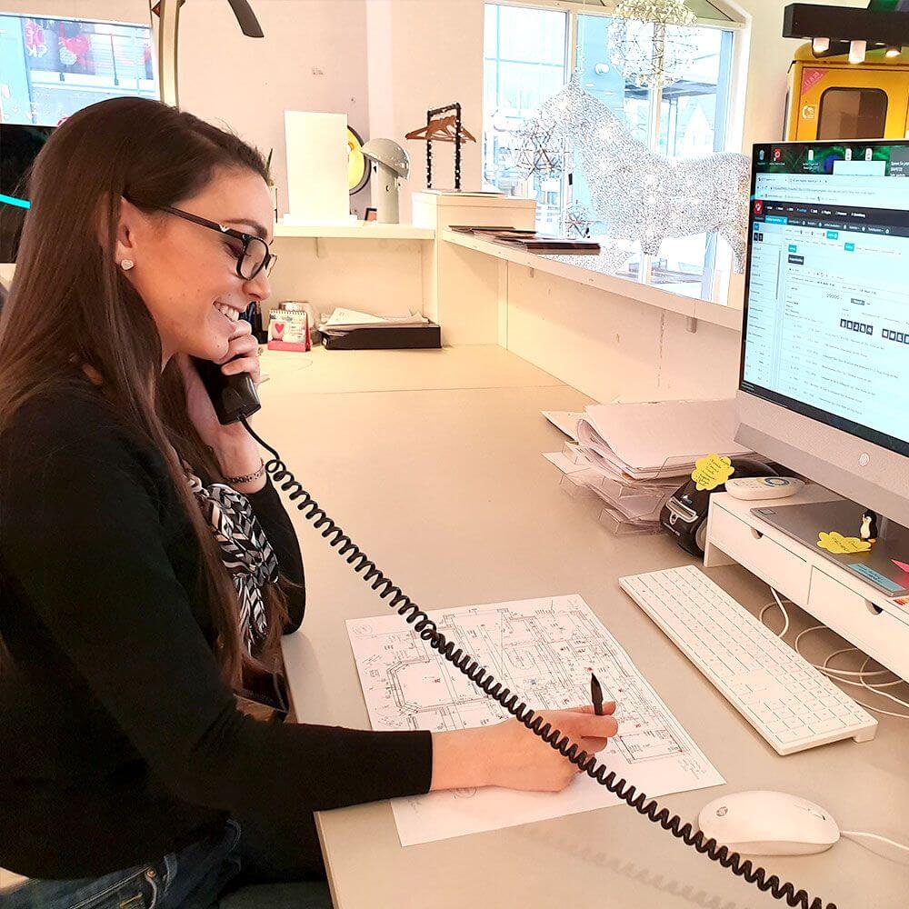 Frau am Telefon, arbeitet an kreativen Lichtkonzepten, umgeben von Büroausstattung und Notizen.