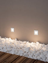 Krypton LED Außenwandeinbauleuchte quadratisch mit 3000K Weißlicht, IP54, an Wand mit Kies.