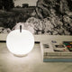 Kundalini Glas Tischlampe Kushi Ø16cm auf moderner Tischoberfläche mit Zeitschriften im Hintergrund.