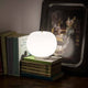Kundalini LED Tischlampe Kushi auf einem Bücherstapel, mit sanftem Licht und künstlerischem Hintergrund.