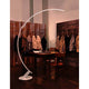 Kundalini LED Bogen-Stehlampe Kyudo Dimmbar in eleganter Umgebung mit einem Tisch und Jacken im Hintergrund.
