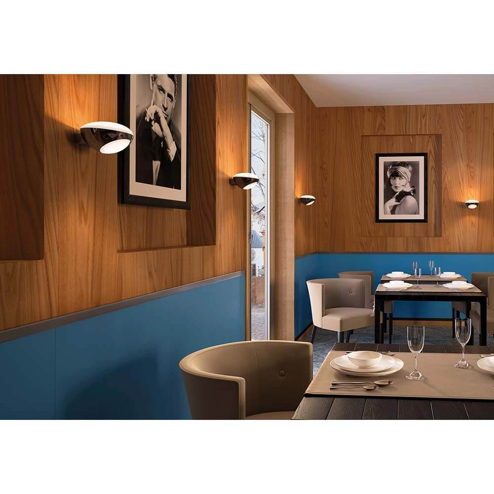 Kundalini LED Wandleuchte Tua Dimmbar in modernem Restaurant-Interieur mit Holz- und blauen Wänden.