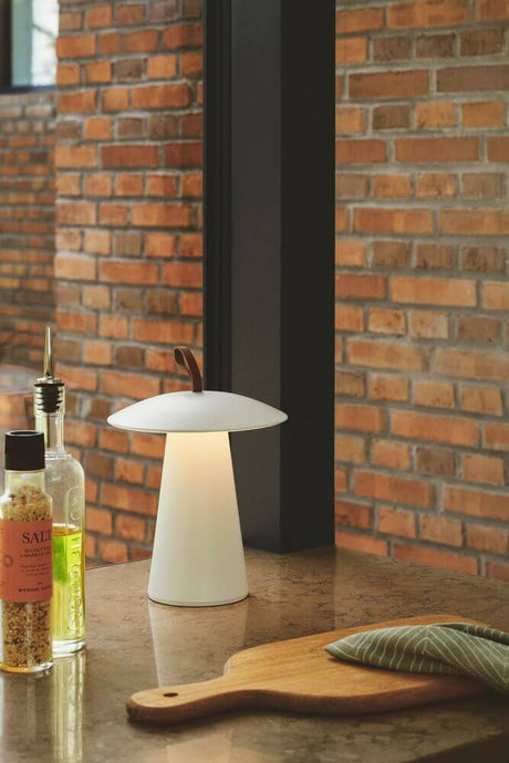 LED Akkuleuchte Ara To-Go 2 IP54 auf einem Tisch neben Gewürzen und einem Holzbrett in modernem Ambiente.