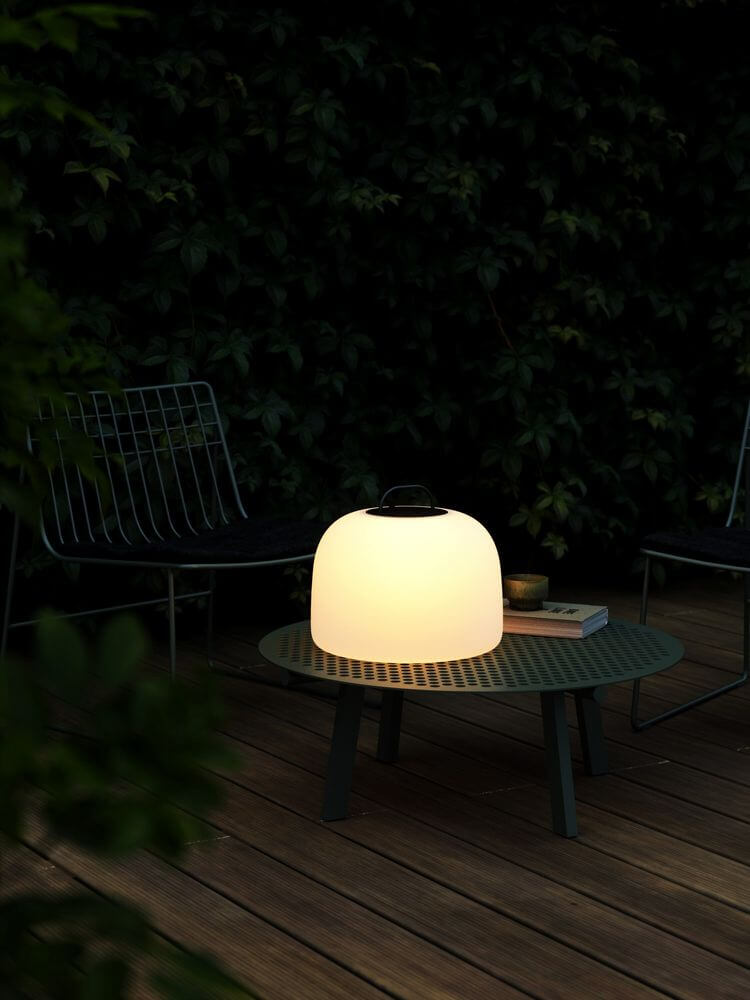 LED Akkuleuchte Kettle To-Go 36 IP65 auf einem Tisch im Freien, ideal für stimmungsvolle Beleuchtung.