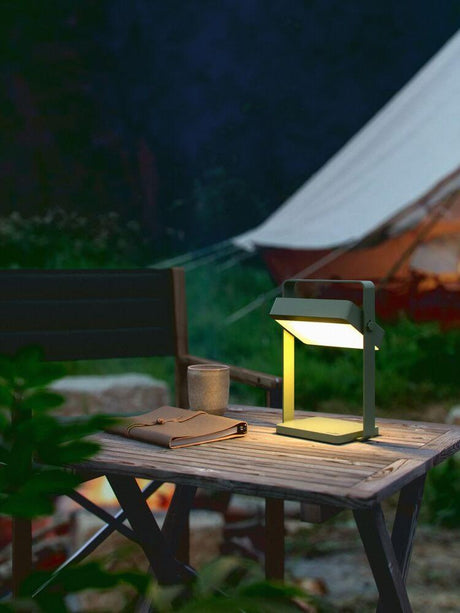 LED Akkuleuchte Saulio Solar IP44 auf einem Tisch neben einer Campingliege bei Nacht.